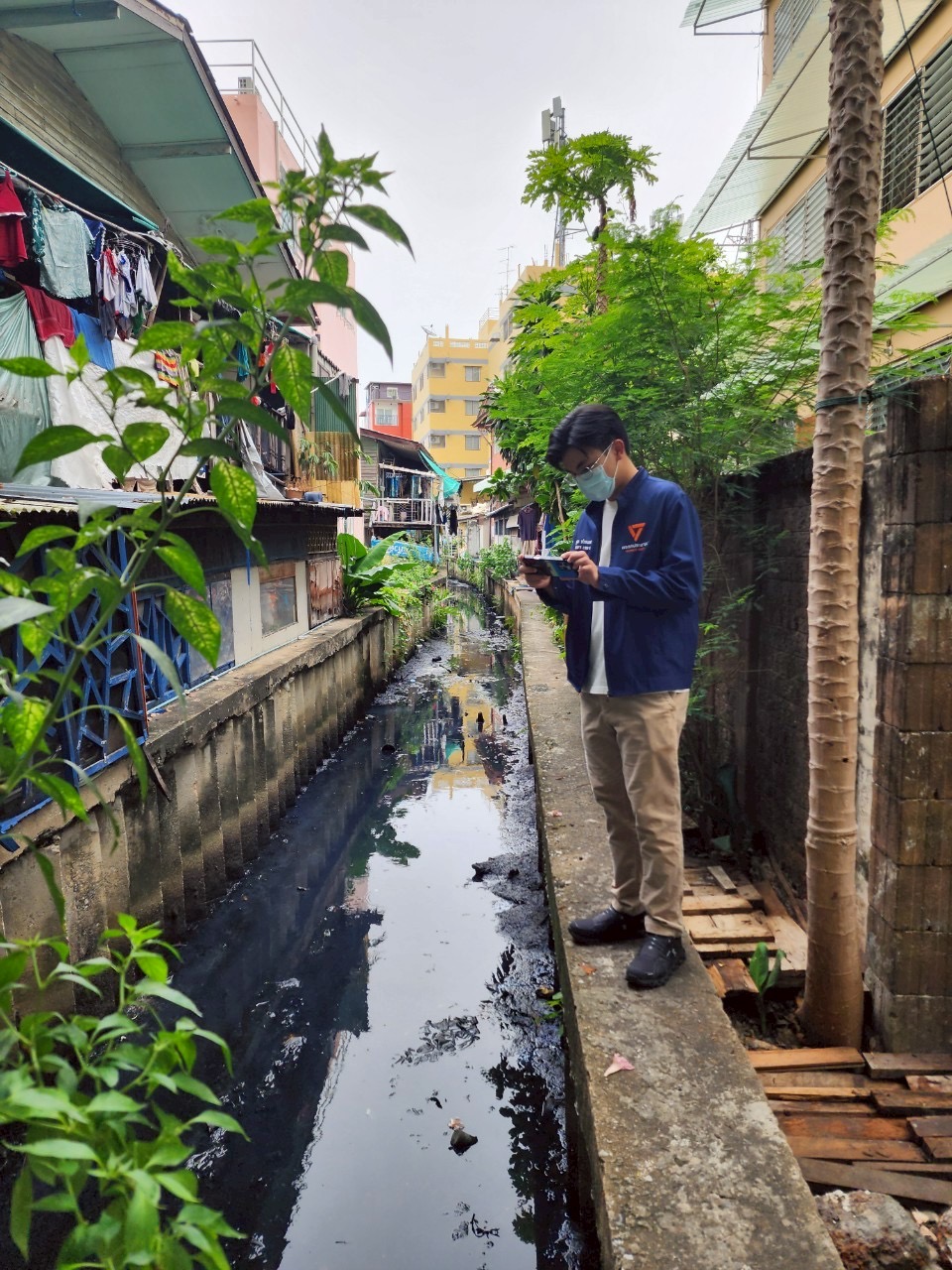 Thanapat records conditions at a drainage canal beside a Bangkok community during a field visit